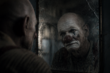 Eine Person steht vor einem beschlagenen Spiegel; darin ein verwischtes Clownsgesicht. Der Blick ist ruhig, der Raum kühl und leer.